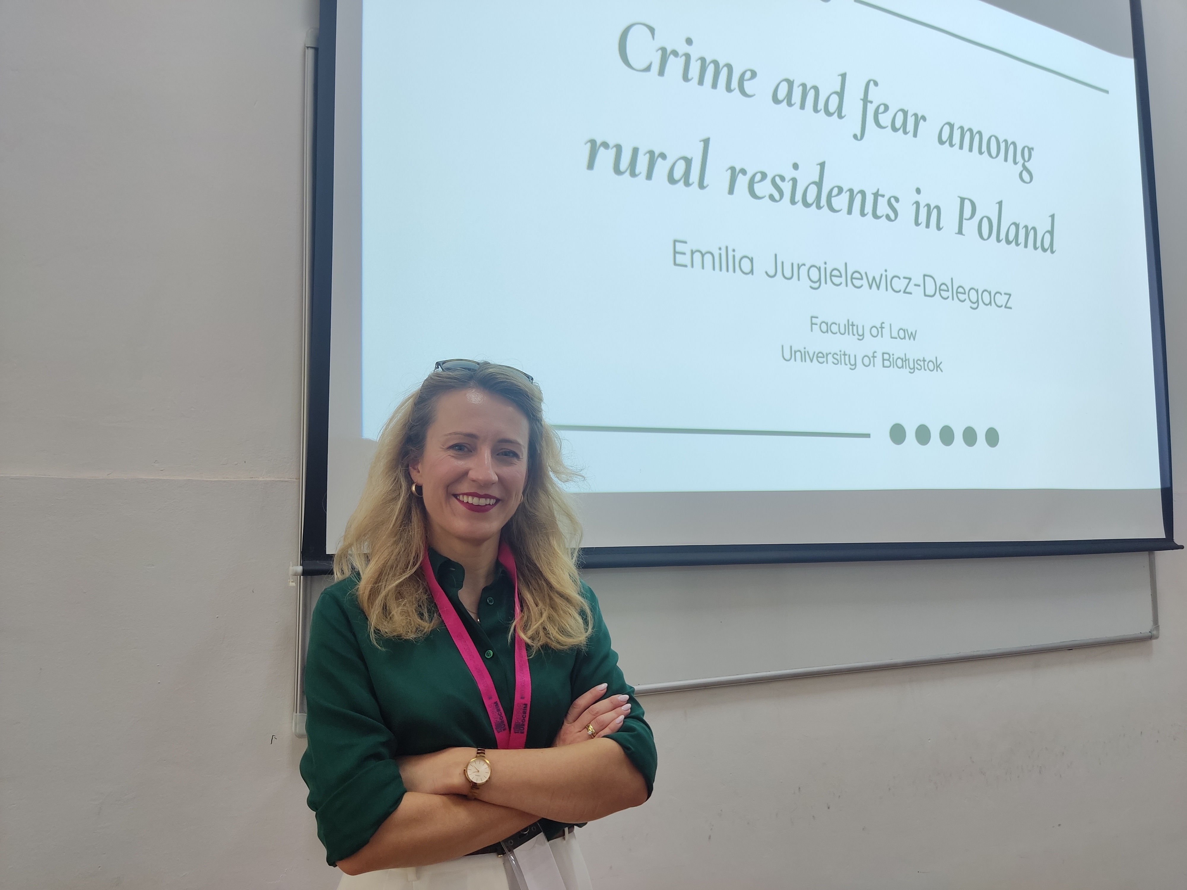 Emilia Jurgielewicz-Delegacz stojąca na tle wyświetlającej się prezentacji z widocznym tytułem wystąpienia „Crime and fear among rural residents in Poland”.