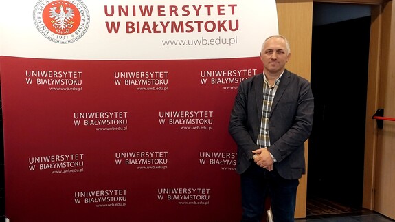 mężczyzna na tle ściany promocyjnej z napisem Uniwersytet w Białymstoku